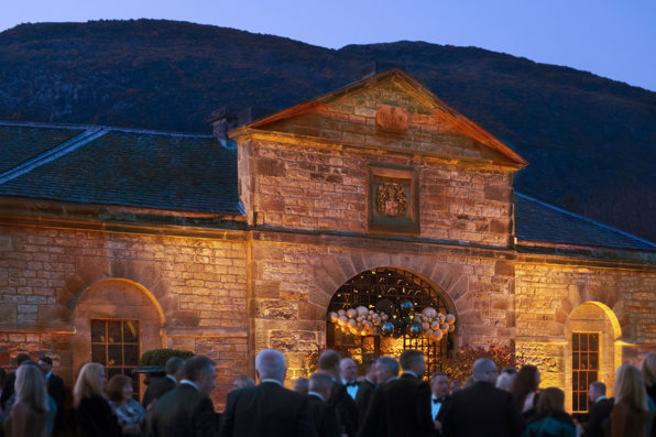 Guests dressed in black tie attire outside The Stables venue in Edinburgh at evening event drinks reception on the lawn at Prestonfield