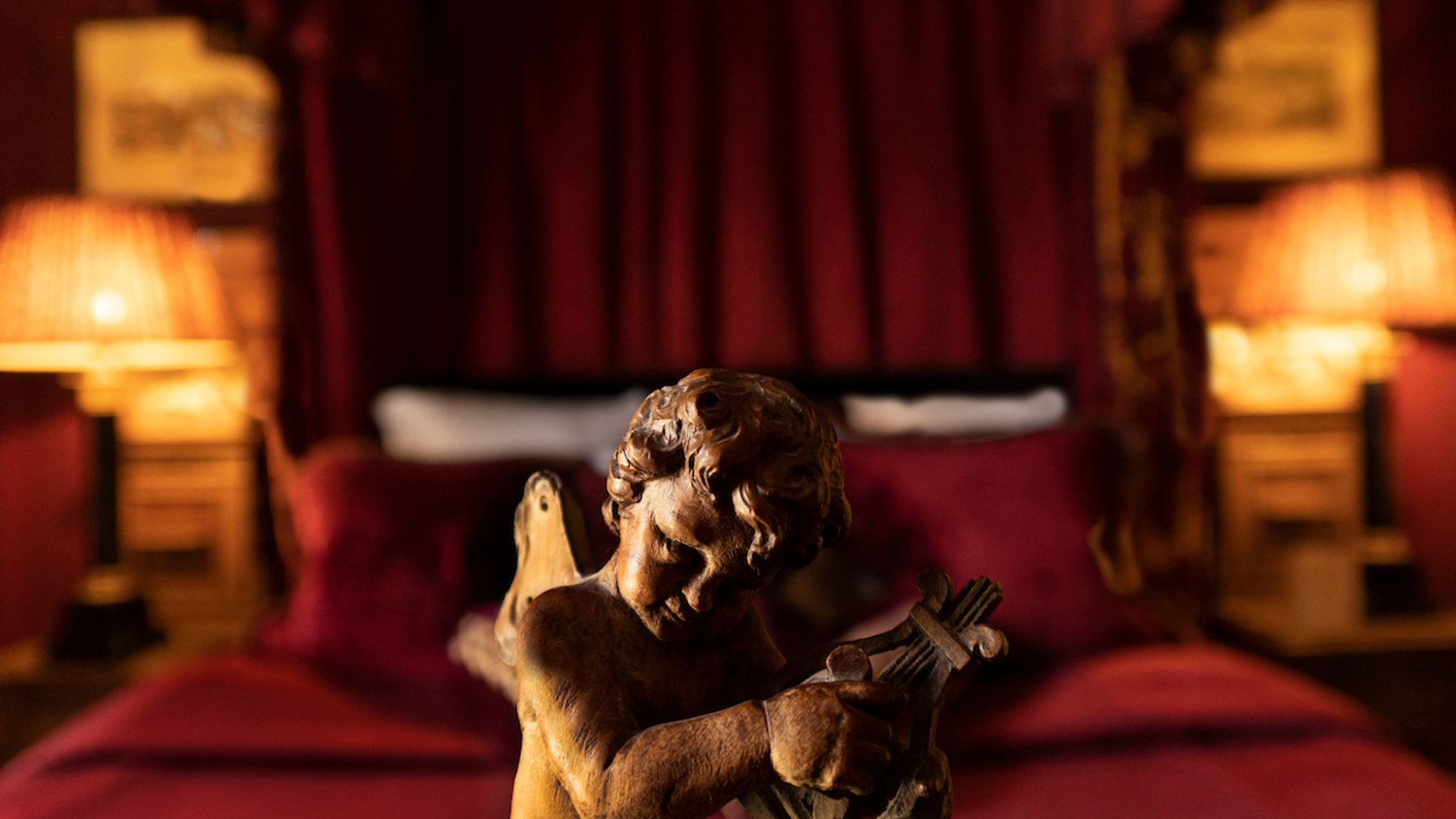 Carved wooden cherub before a grand Edinburgh hotel suite with velvet bedding, antique furnishings, and warm, ambient lighting.