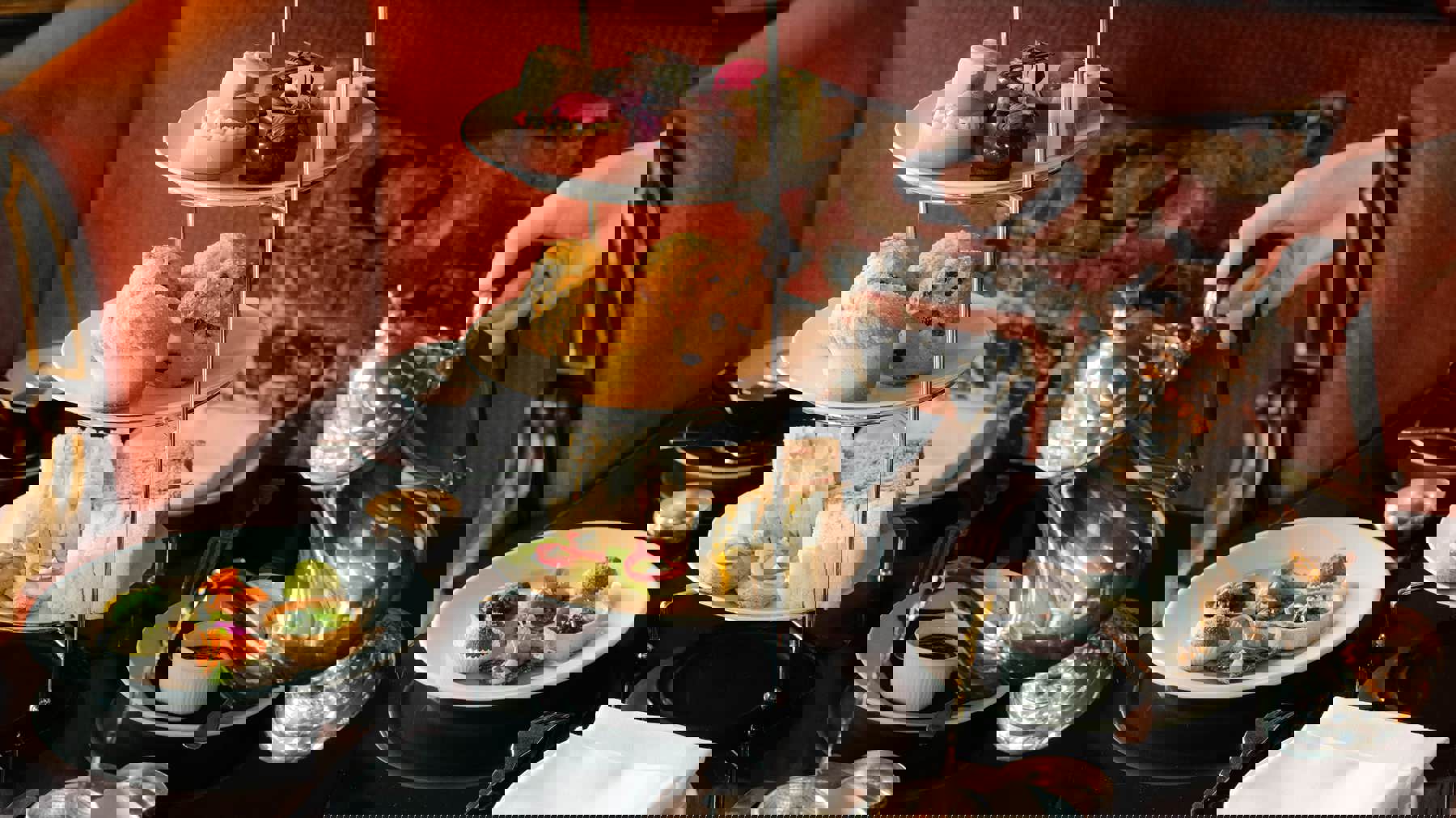 Elegant afternoon tea in Edinburgh served on a three-tier stand at Prestonfield House, featuring sandwiches, scones and pâtisserie as tea is poured at a black-lacquered table in the restaurant’s luxurious setting