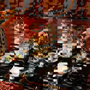 Elegant afternoon tea in Edinburgh served on a three-tier stand at Prestonfield House, featuring sandwiches, scones and pâtisserie as tea is poured at a black-lacquered table in the restaurant’s luxurious setting